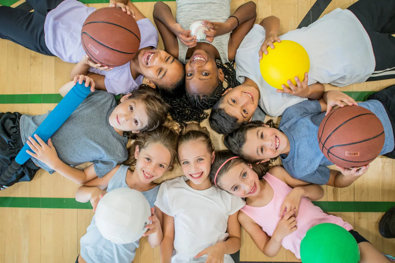 Group of kids on the gymnasium floor holding balls