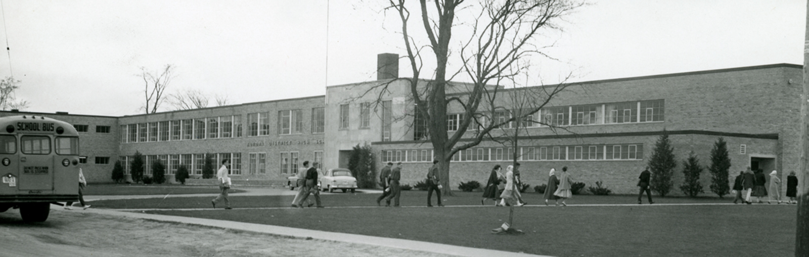 Old black and white picture of Dr. G.W. Williams school, with kids walking towards the school and an old school bus on the left