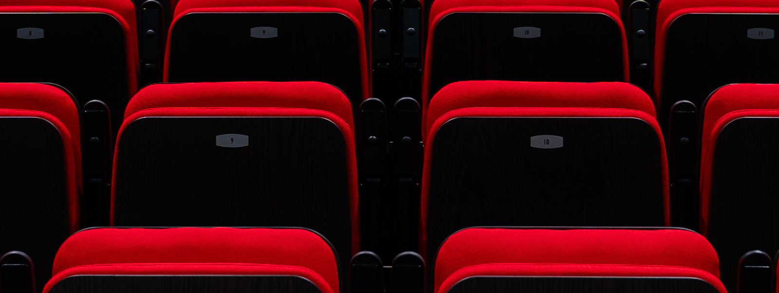 Closeup of closed red theatre chairs in a dark setting