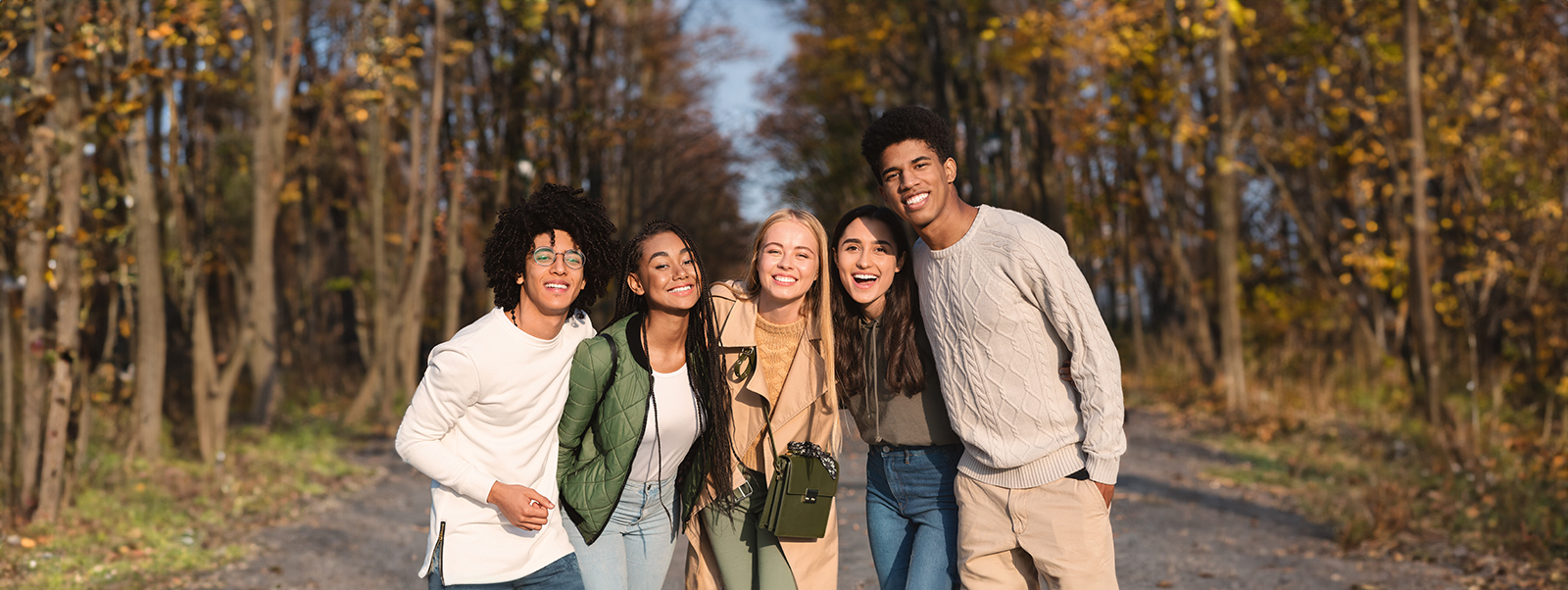 Group of young adults standing side by side in a forest, with trees behind them