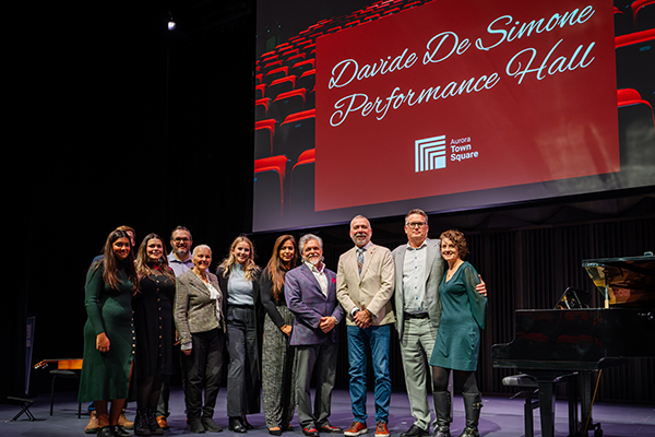 De Simone family on stage with the Mayor, beside a piano and with the space (family) name on a large screen behind them.