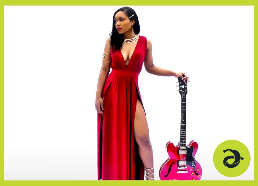 Woman wearing a red dress stands with her pink guitar