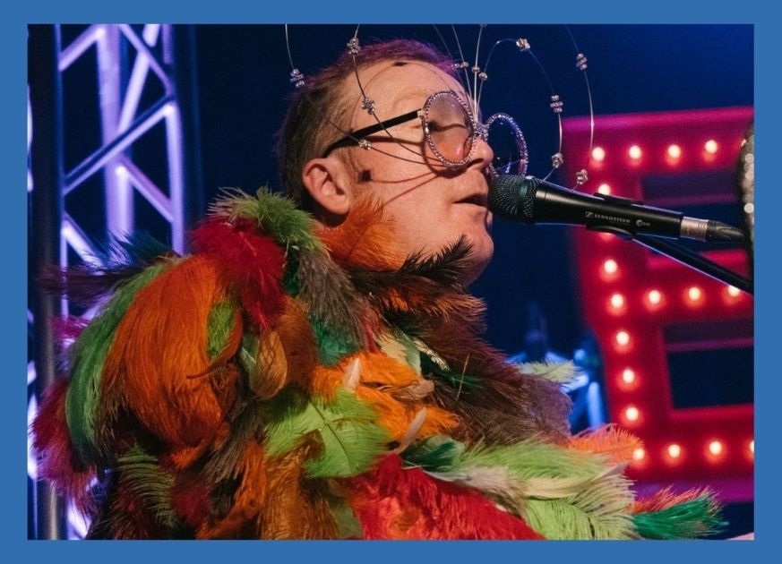 Man dressed like Elton John singing into a microphone