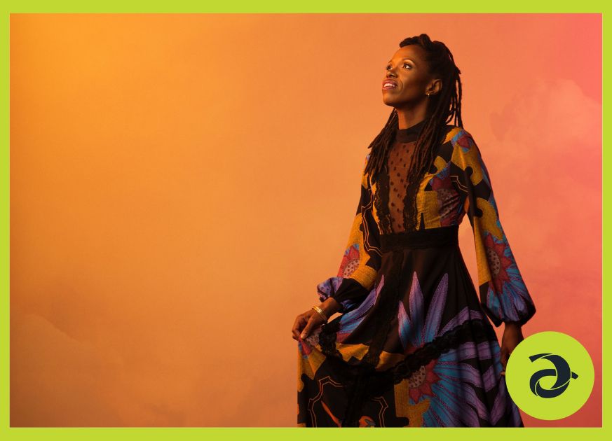 A woman on stage, looking to the sky and surrounded by colourful fog