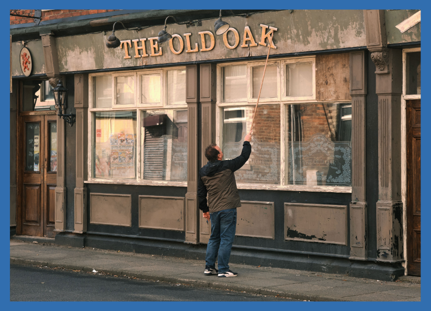 Man putting up a sign on an old building that says The Old Oak