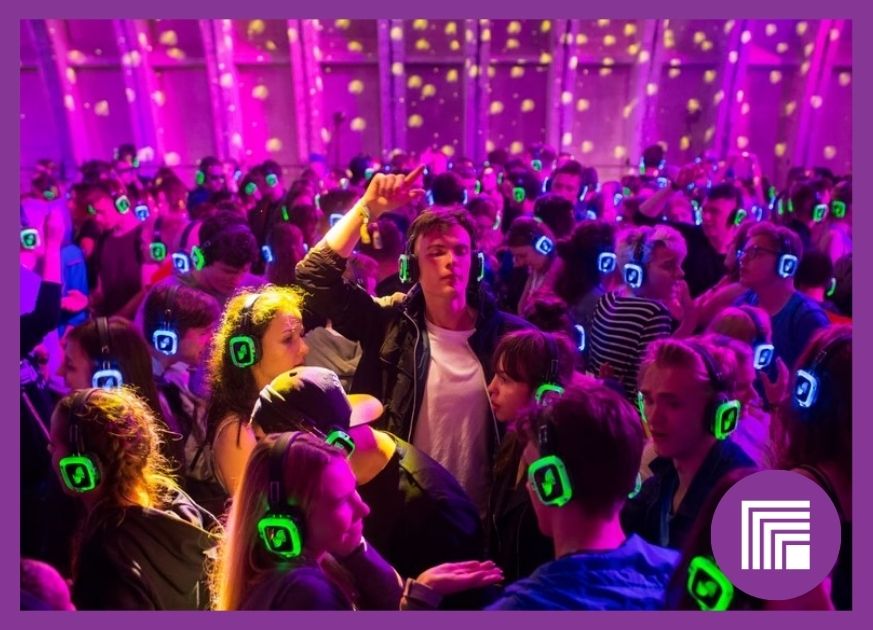 Many people in a vibrant purple themed room, with green headphones on